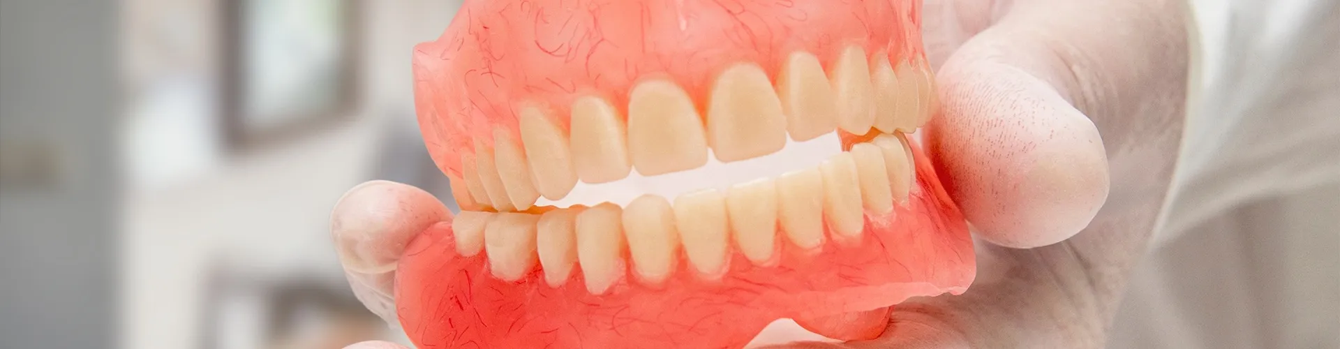 gloved hand holding a pair of dentures