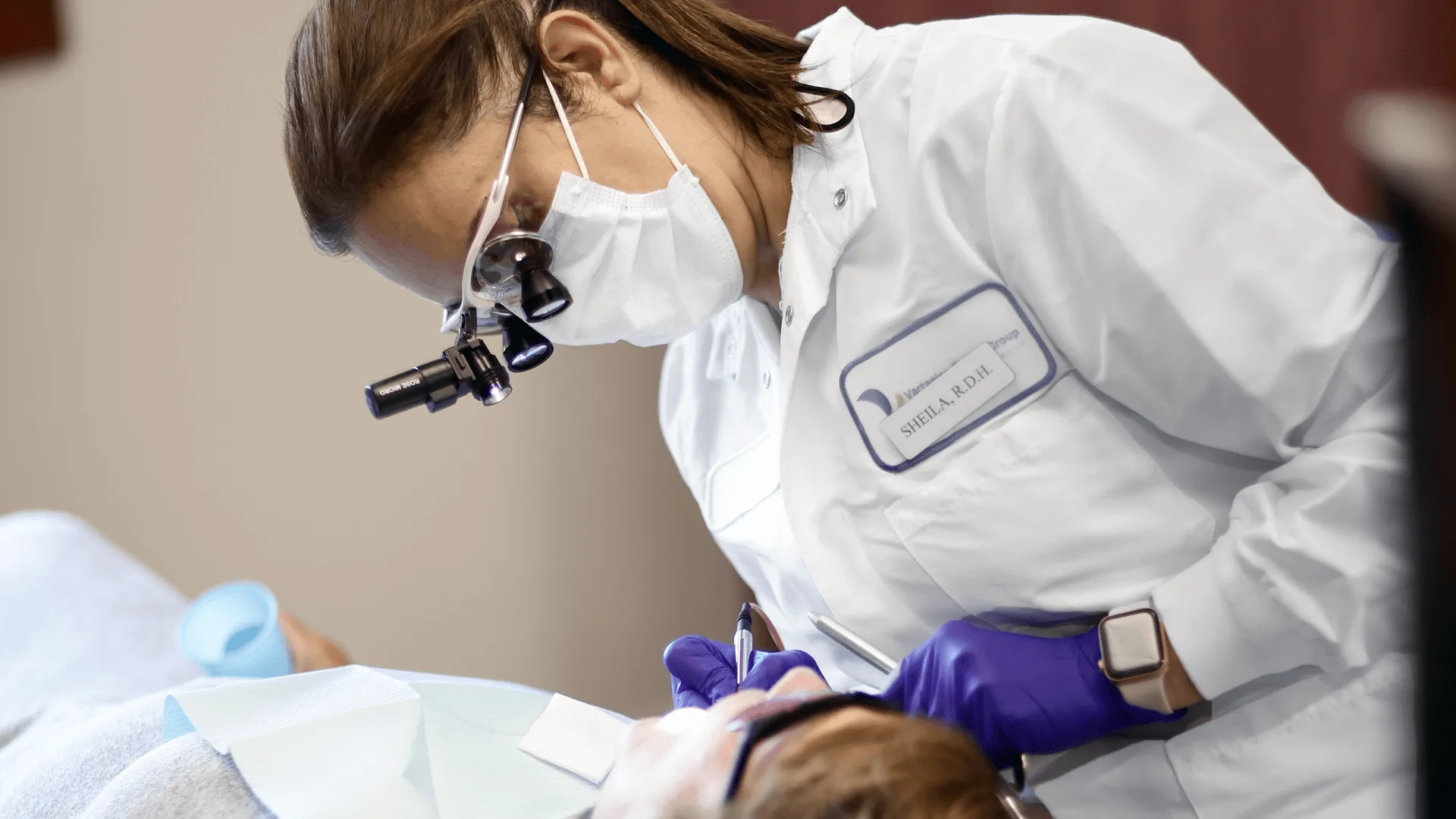 A dental hygienist, Sheila R.D.H., performing a detailed examination on a patient, using advanced dental tools and magnification, focusing on treating and managing gum disease effectively.