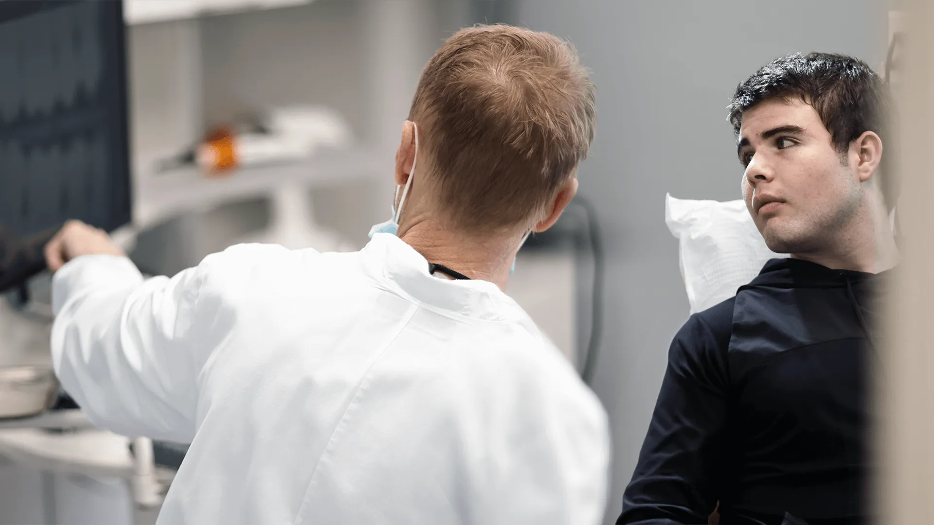 A dentist in a white coat is discussing dental care with a young male patient, who appears concerned. The setting is a modern dental office, conveying a professional consultation for emergency dental situations.