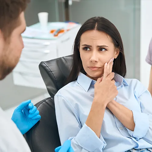 woman holding her cheek in pain in front of dentist