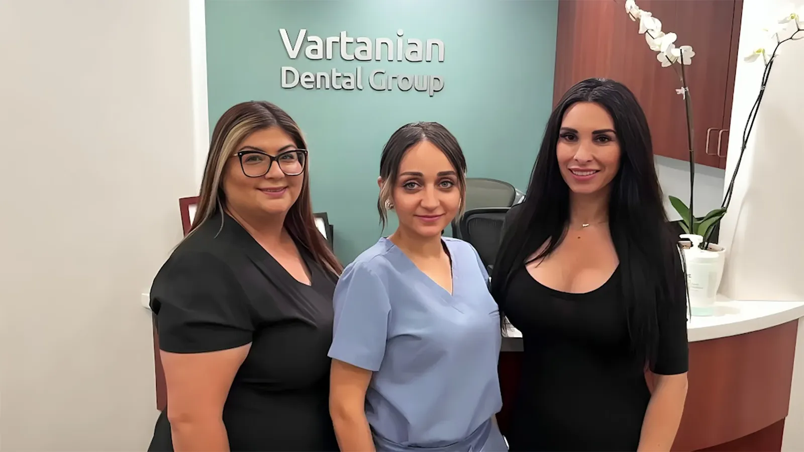 Three women dental assistants smiling at the front desk.