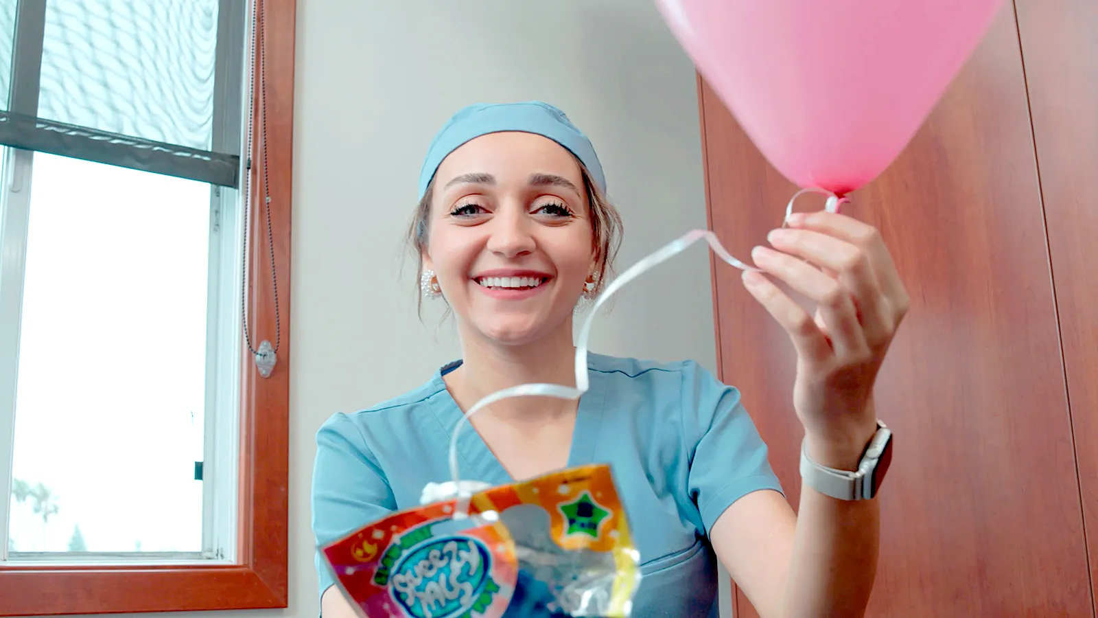 Dentist smiling while holding a pink balloon in her hand.