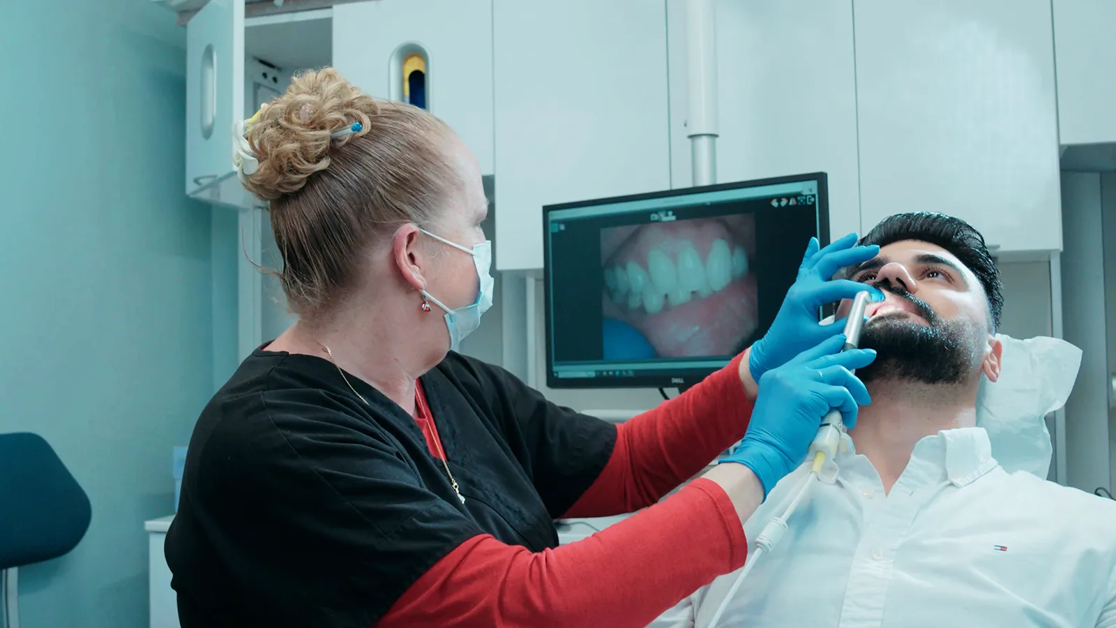 Man lying on a dental chair while the dentist checks his teeth with a camera, displaying the image on a screen.