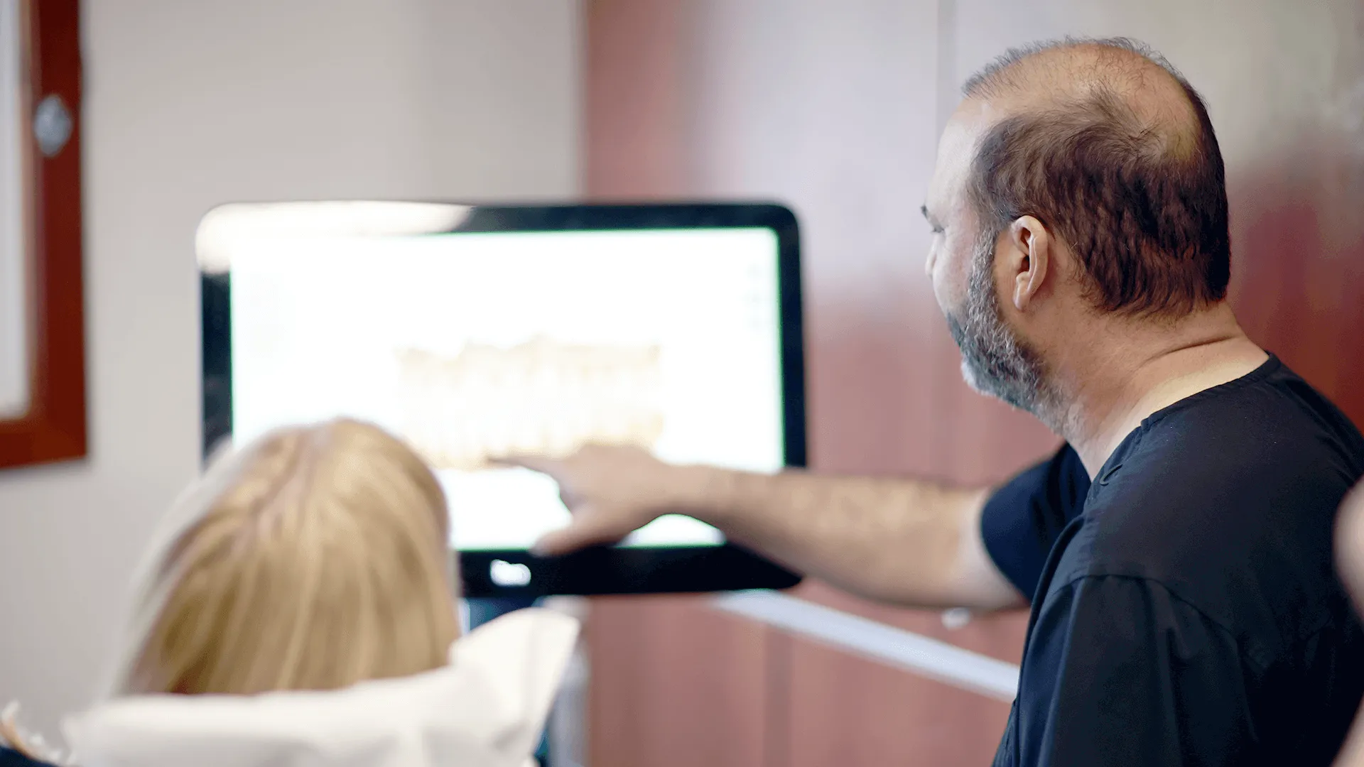 Dr. James Vartanian pointing to a digital X-ray on a monitor during a dental consultation with a female patient, highlighting areas of concern and treatment plans.